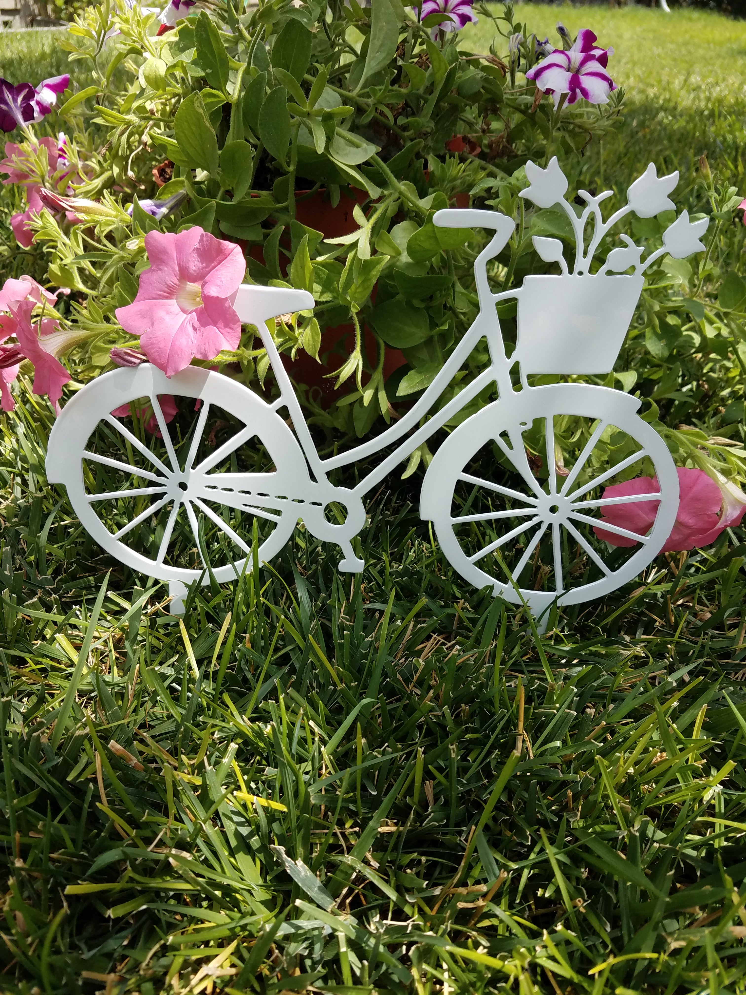 White powder coated bicycle with tulips in basket on stakes in flower bed.